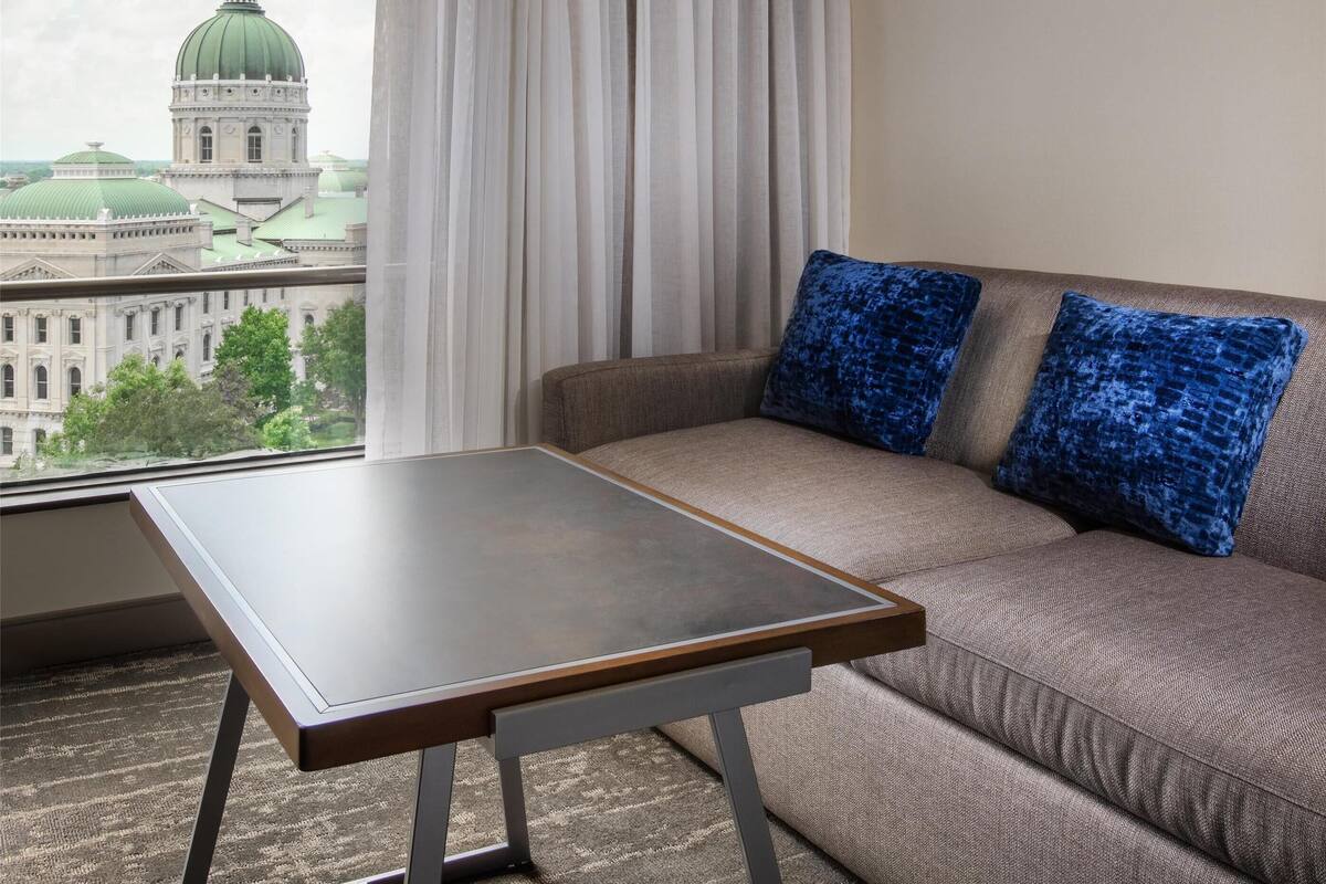 Une chambre d’hôtel moderne avec un canapé, une petite table et une vue sur le paysage urbain, notamment un bâtiment avec un dôme vert.
