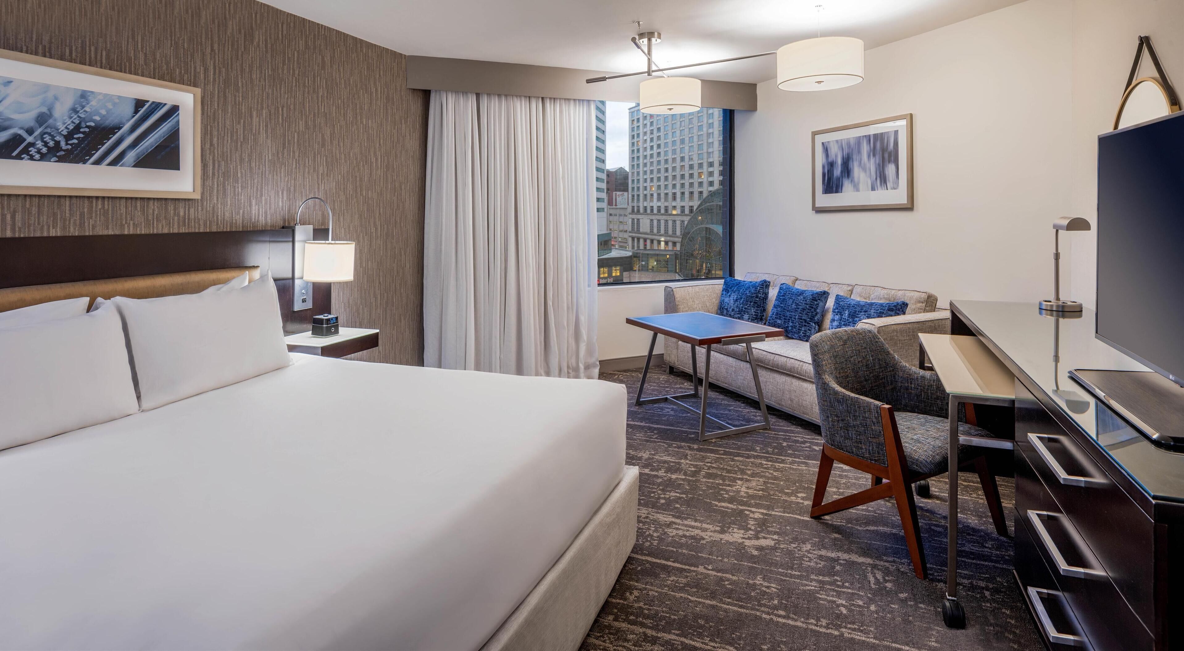 Habitación de hotel con cama, escritorio, silla, televisor y vistas a la ciudad.