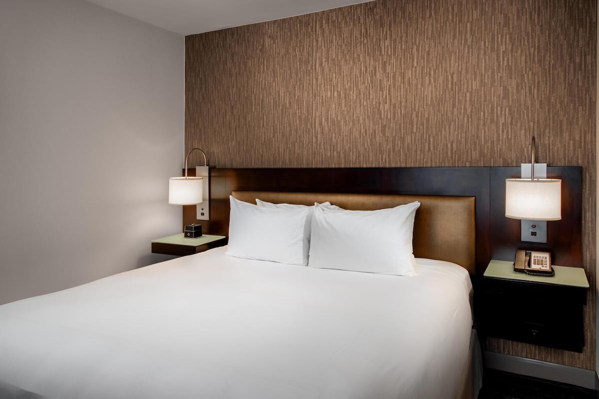 Une chambre d’hôtel avec un grand lit, deux tables de chevet avec des lampes et une tête de lit en bois.