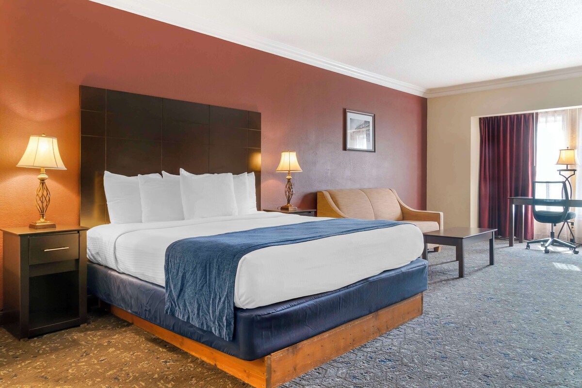 A hotel room with a large bed, two bedside tables with lamps, a chair, and a desk.