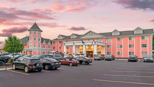 Un hotel con un estacionamiento lleno de coches, una torre destacada y una amplia fachada.