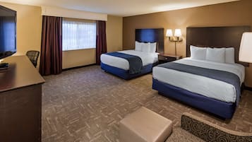 A hotel room with two beds, a desk, a TV, and a window with curtains.