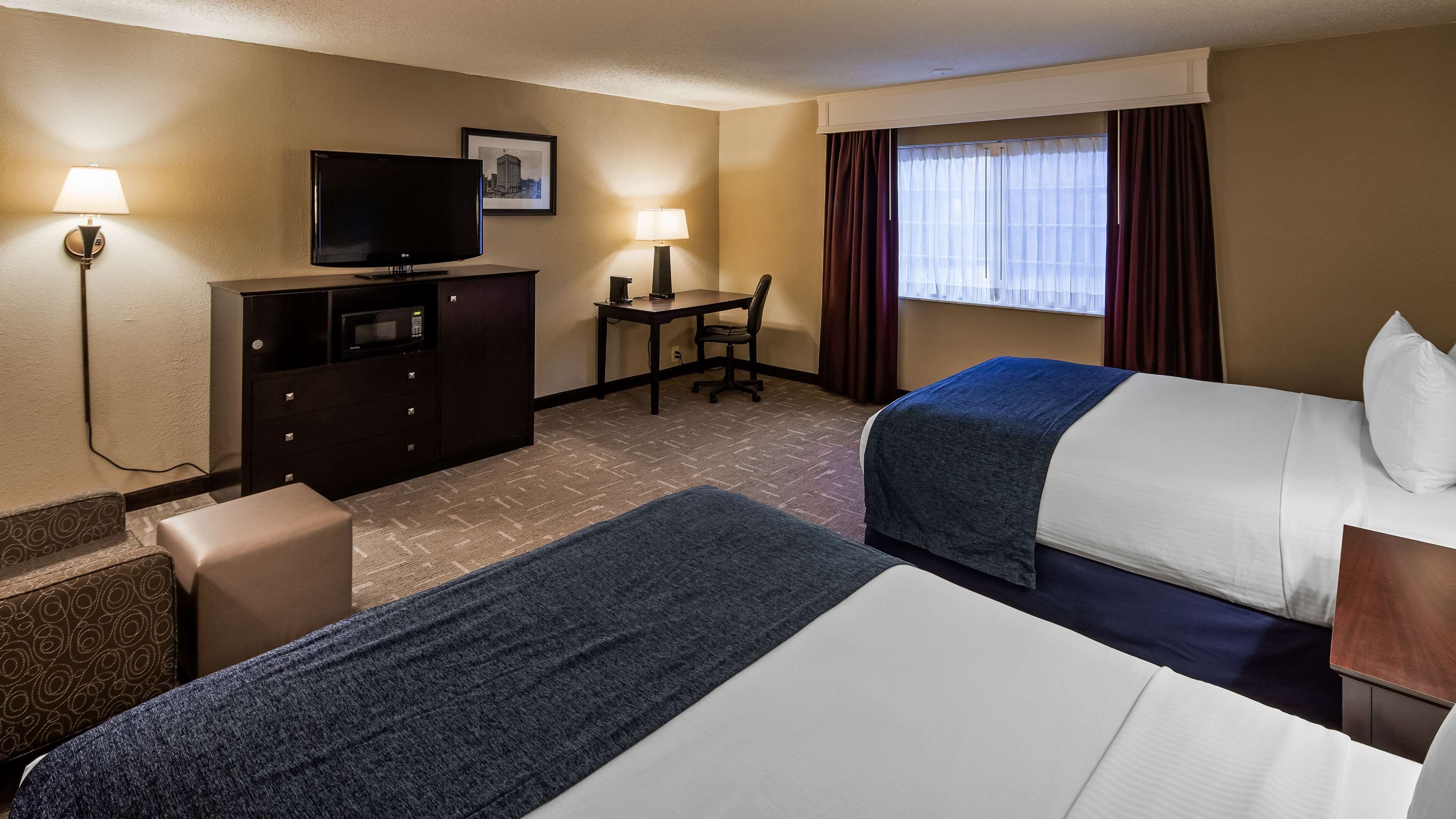 A hotel room with two beds, a desk, a television, a chair, and a small table.