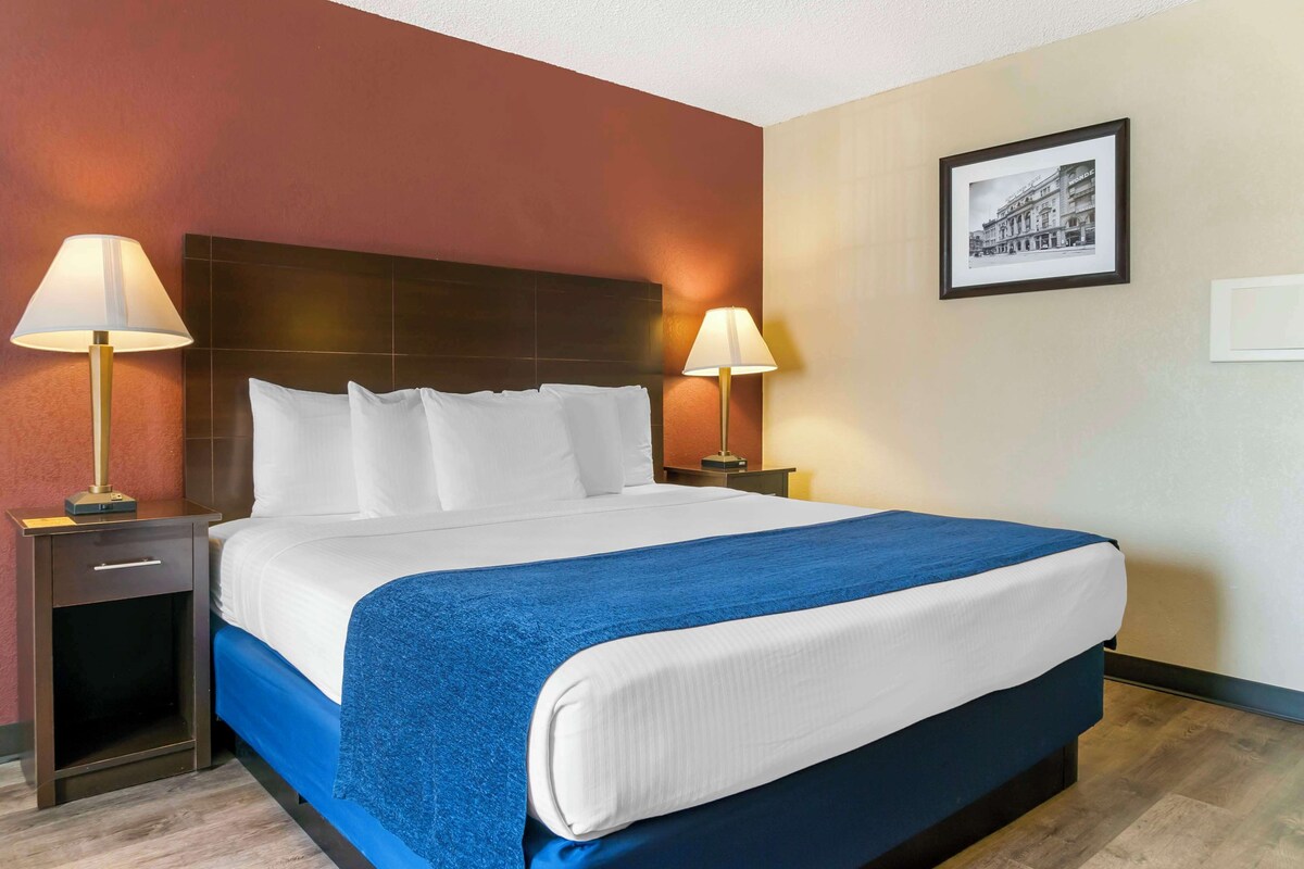 A hotel room with a large bed, two bedside tables with lamps, a framed picture on the wall, and a wooden floor.