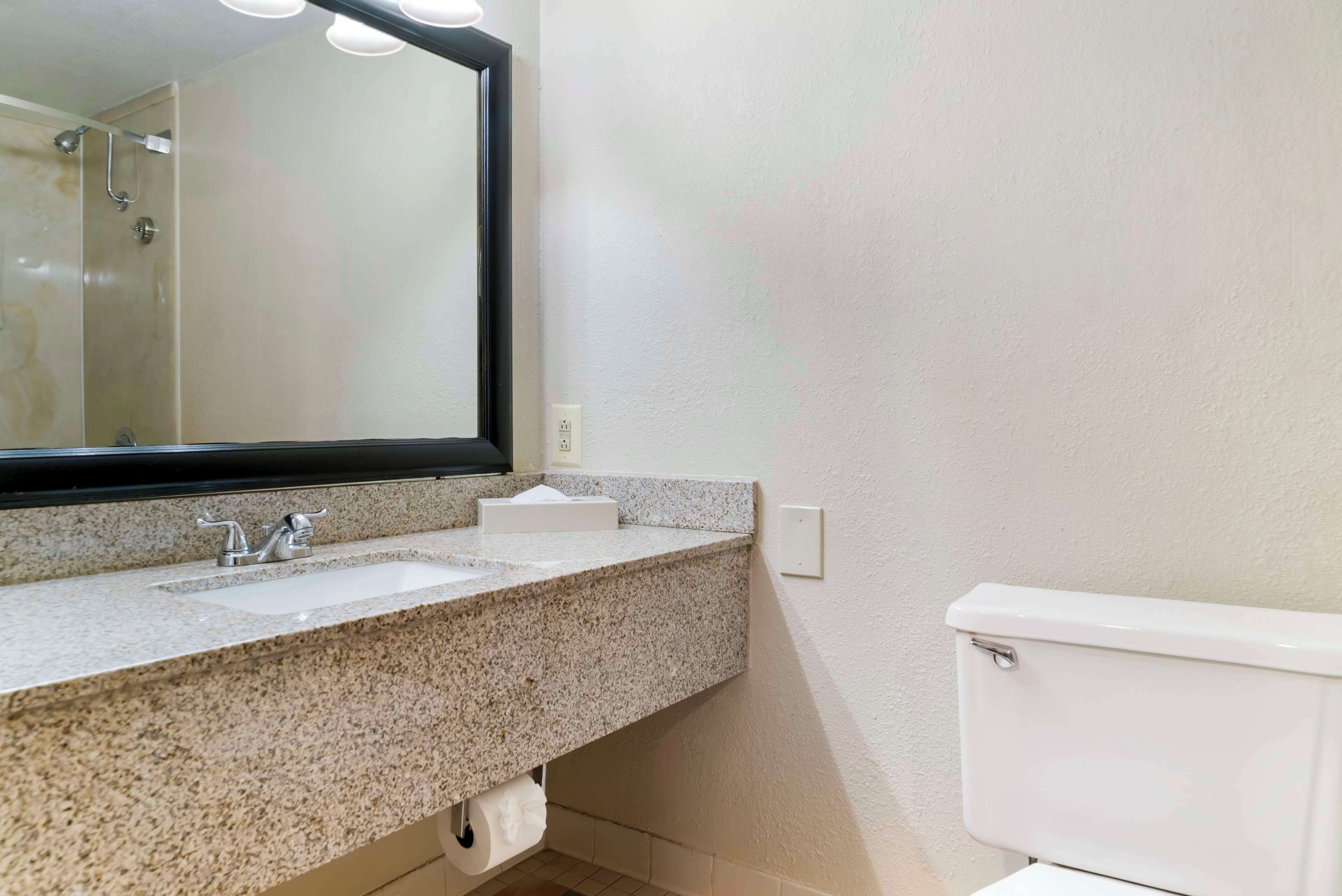 A bathroom with a granite countertop, two sinks, a mirror, and a toilet.