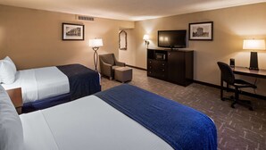 Habitación de hotel con dos camas, un escritorio, una silla, un televisor y una lámpara.