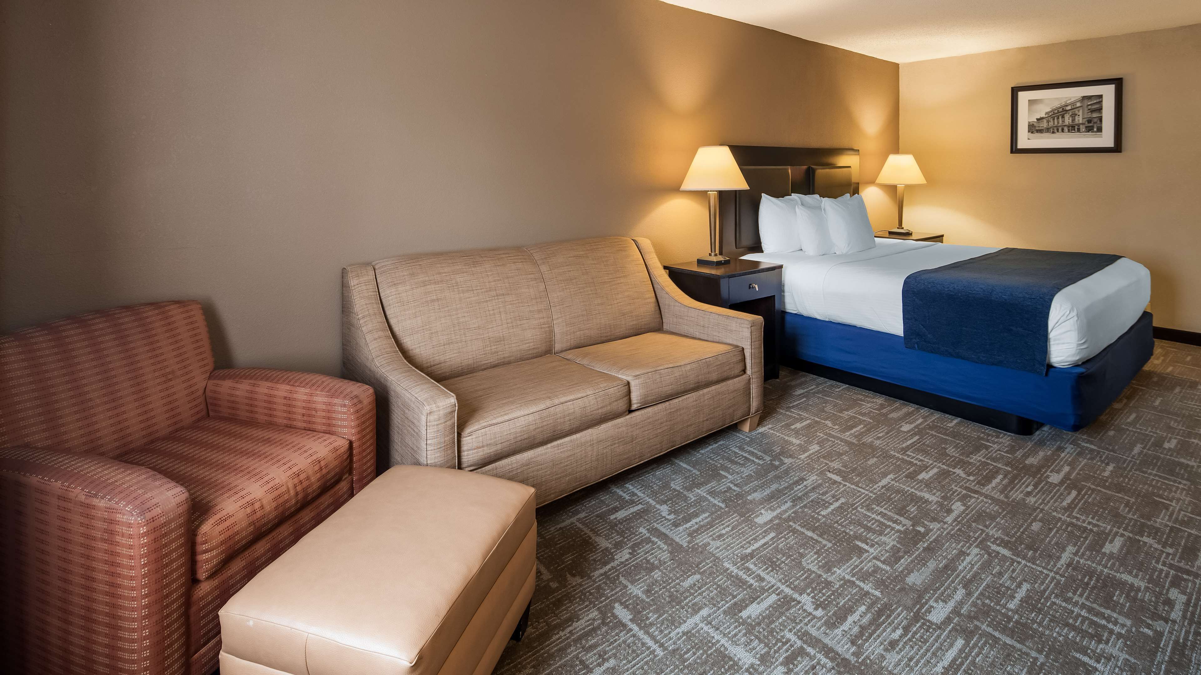 Une chambre d’hôtel avec un lit, un canapé, une chaise et une petite table avec une lampe.