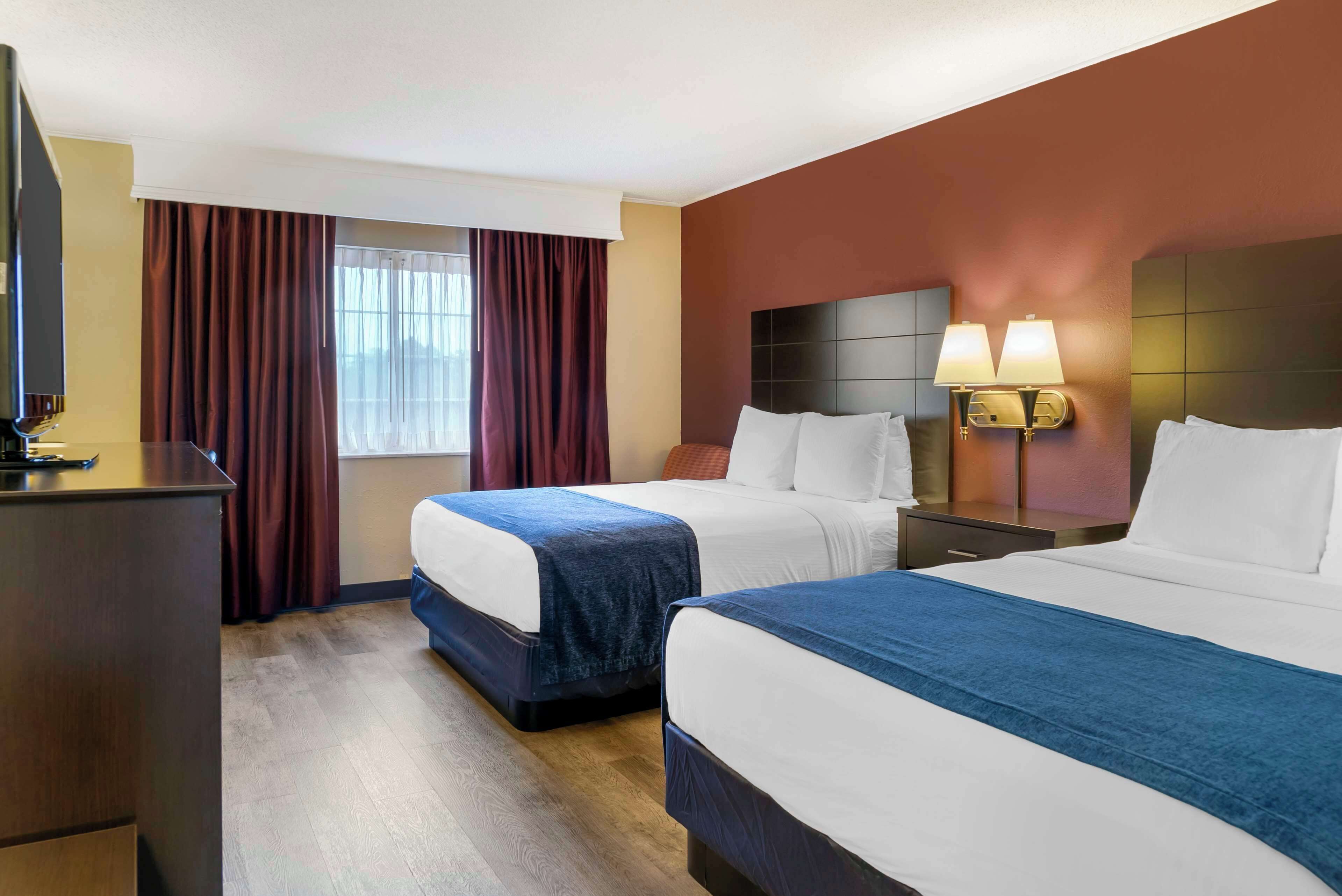 A hotel room with two beds, a desk, a television, and a window with curtains.