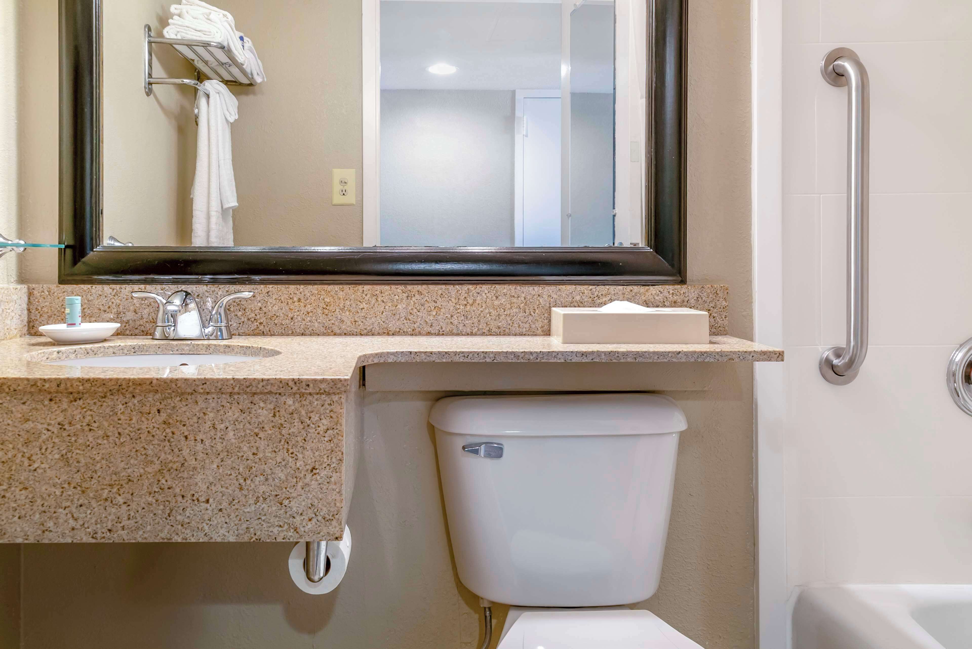 A bathroom with a sink, mirror, toilet, and grab bar.