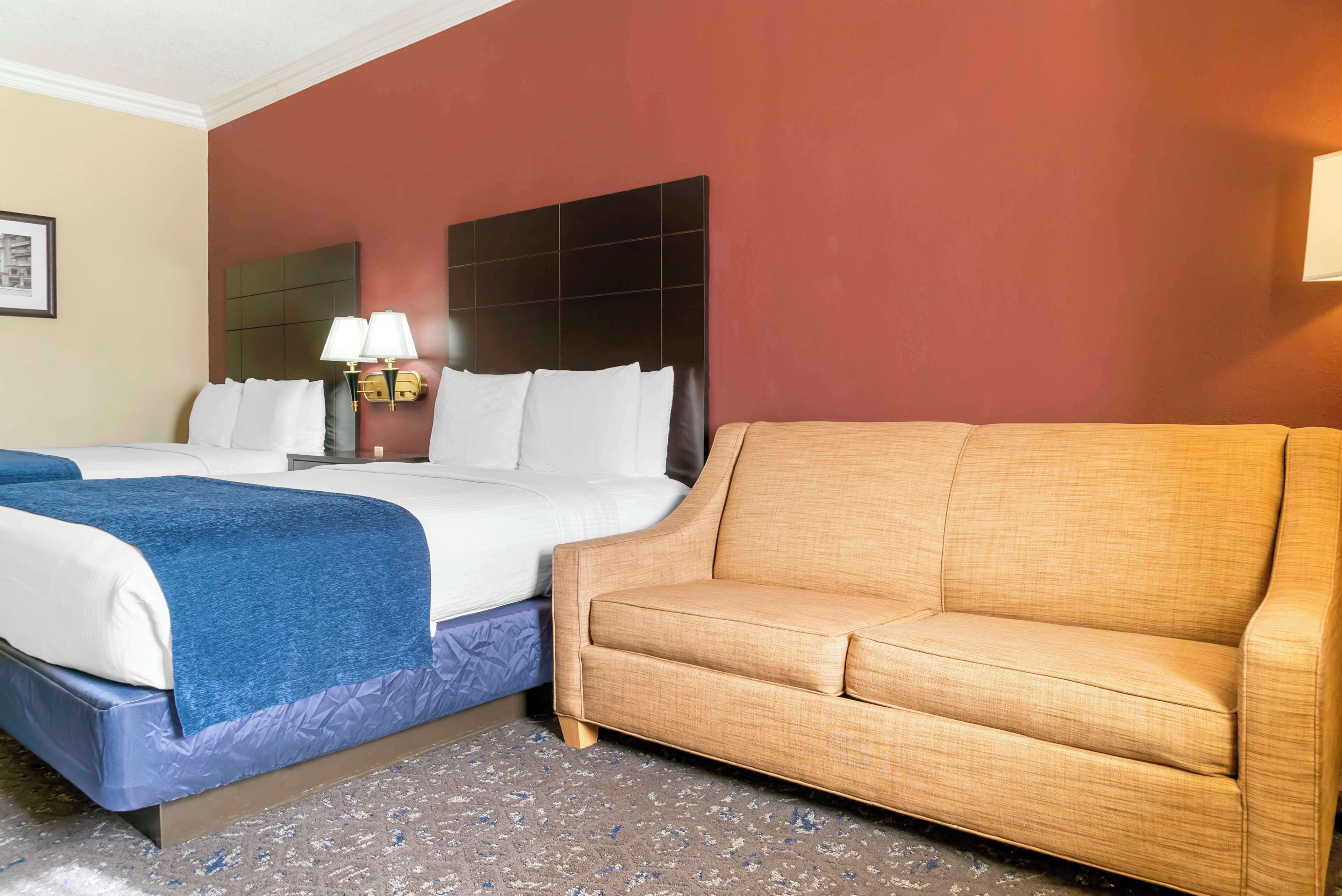 Ein Hotelzimmer mit einem Bett, zwei Nachttischen mit Lampen, einem beigen Sofa und einem gemusterten Teppich.