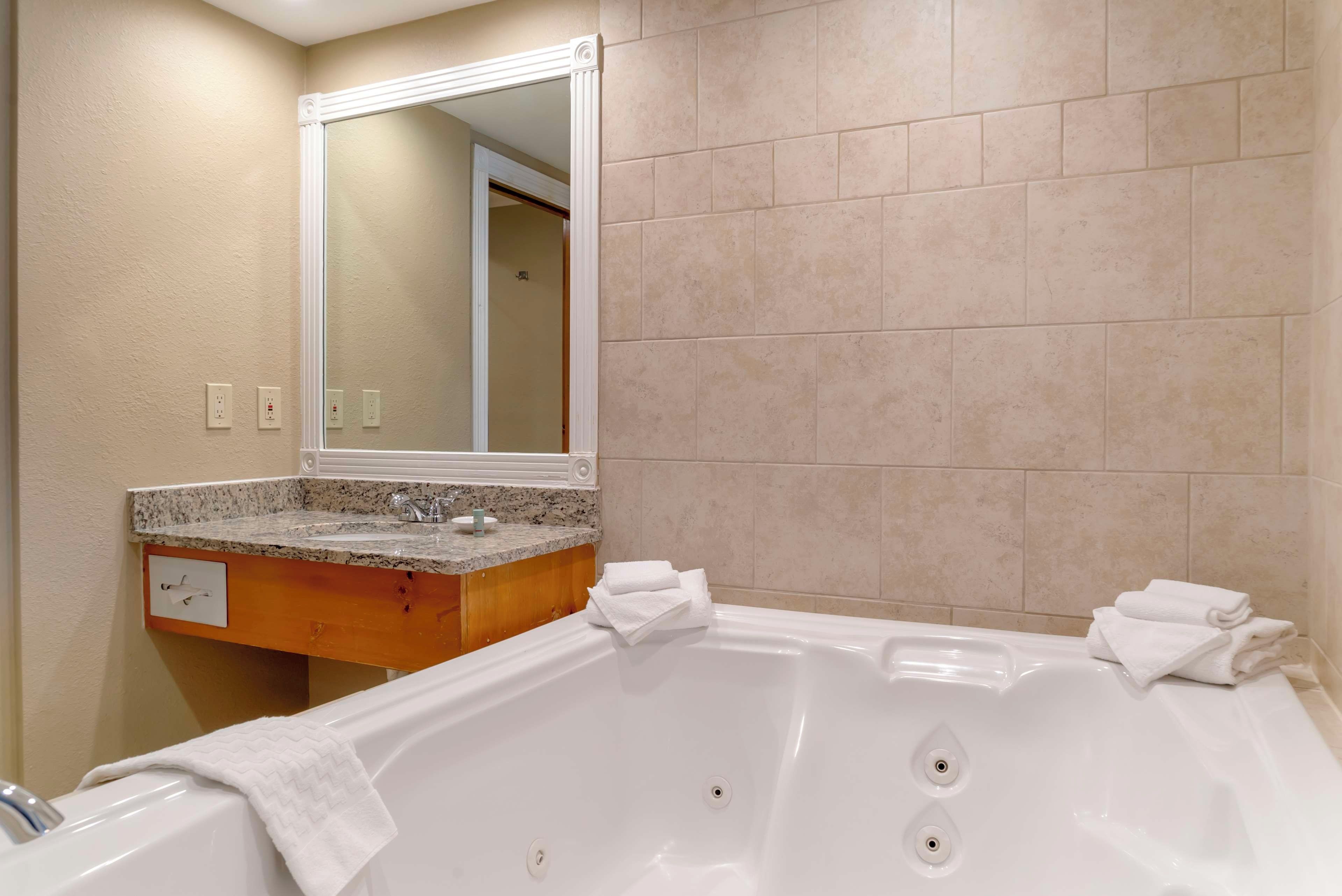A bathroom with a bathtub, a vanity with a mirror, and beige tiled walls.