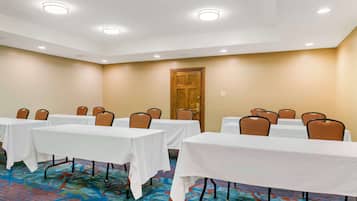 A conference room with tables and chairs, a wooden door, and a patterned carpet.