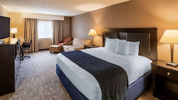A hotel room with a large bed, two bedside tables with lamps, a desk with a chair, and a window with curtains.