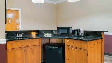 Una cocina con armarios de madera, encimera negra, microondas, cafetera y cubo de basura.