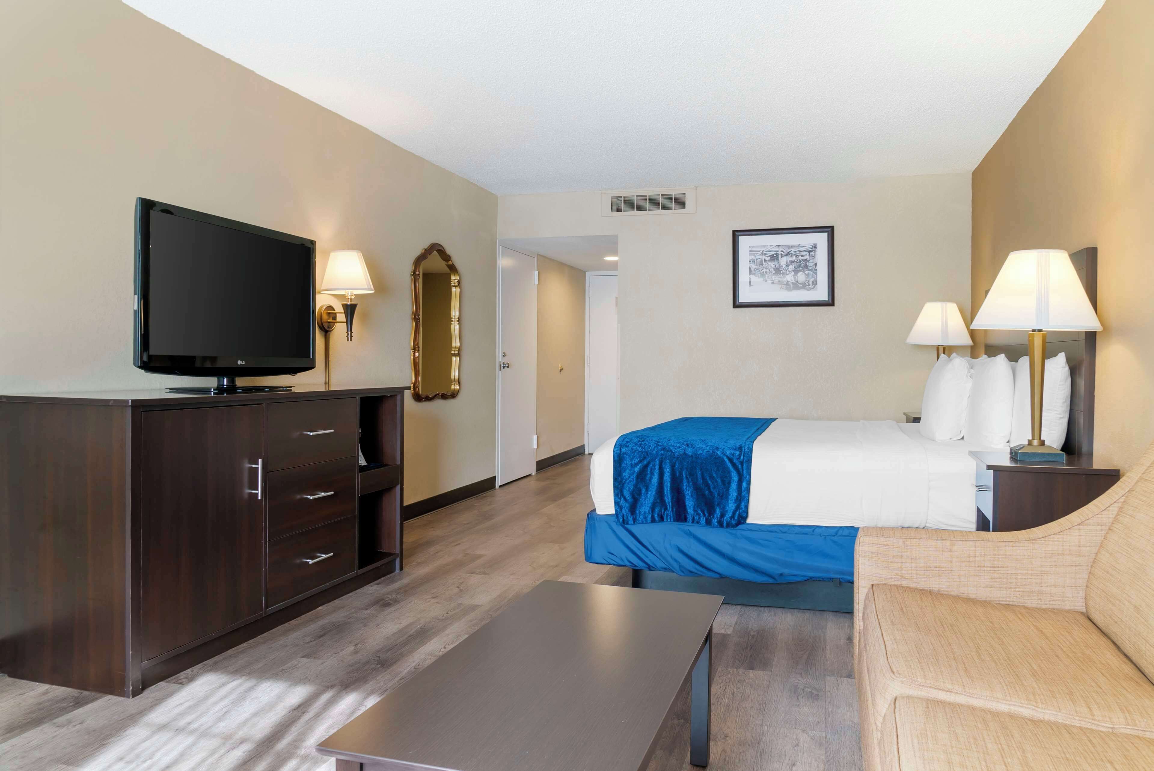 A hotel room with a bed, a TV, a desk, a chair, and a lamp.