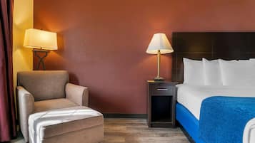 A hotel room with a bed, a chair, a nightstand, and a lamp.