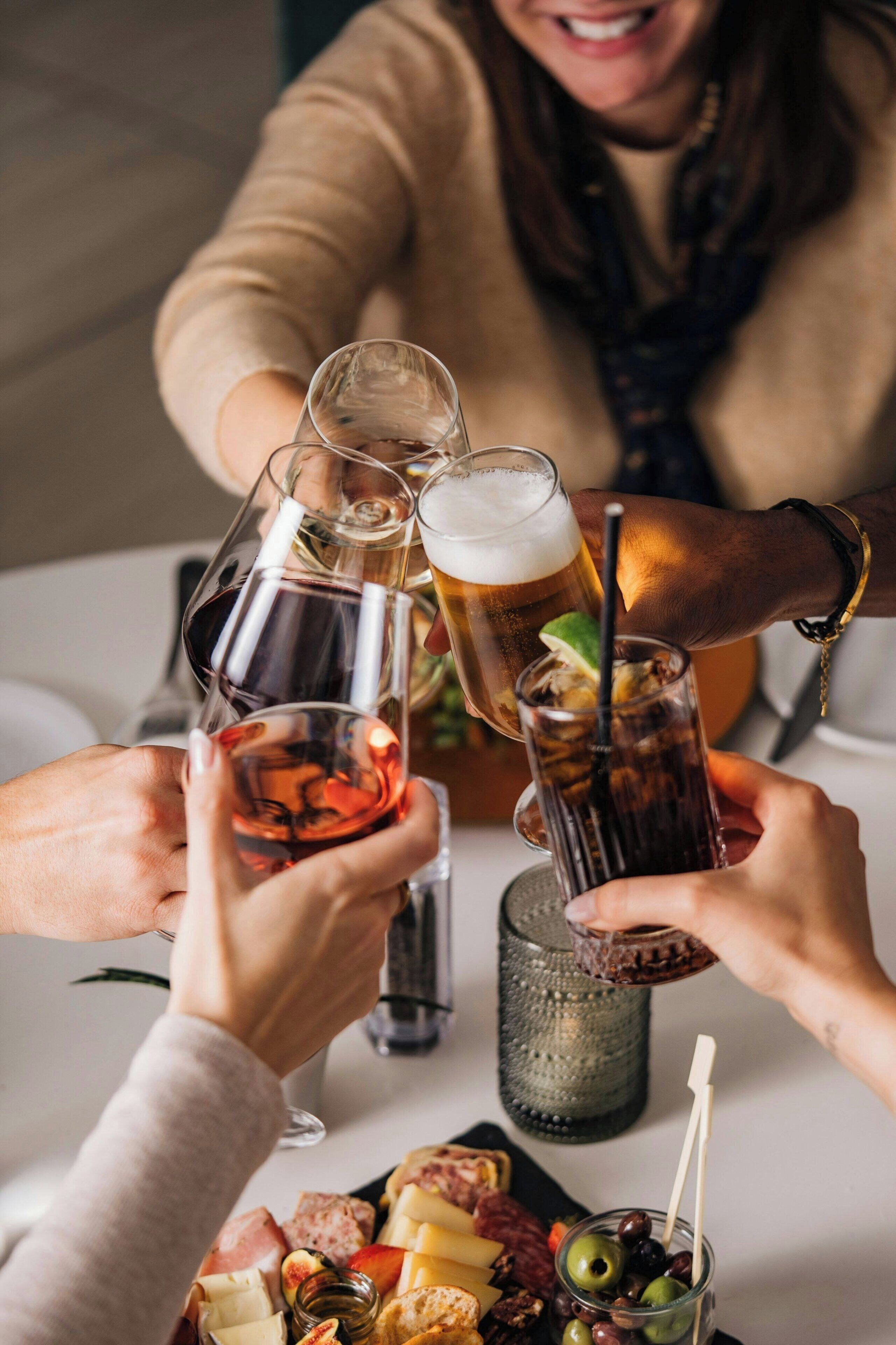 Un groupe de personnes trinquant avec différentes boissons autour d’une table où se trouve une planche de charcuterie.