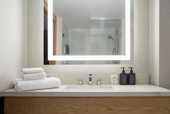 Un baño moderno con un espejo grande, un lavabo blanco y dos botellas de champú.