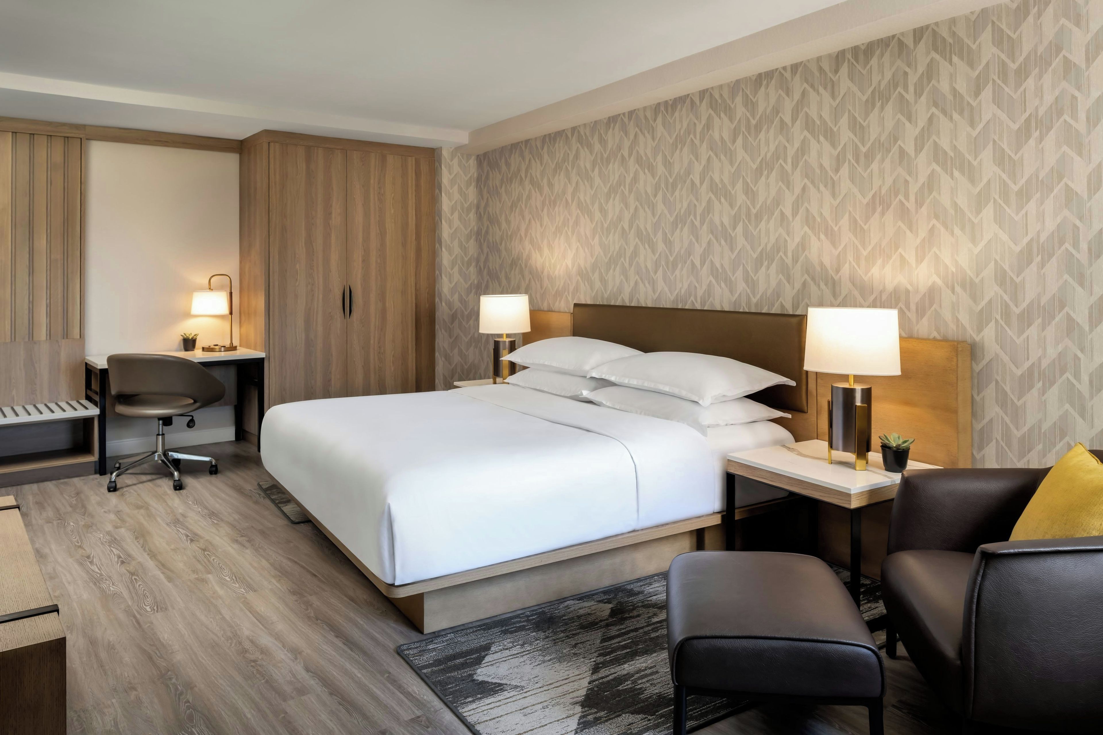 Hotellihuone, jossa on sänky, yöpöydät, työpöytä, tuoli ja pieni matto.