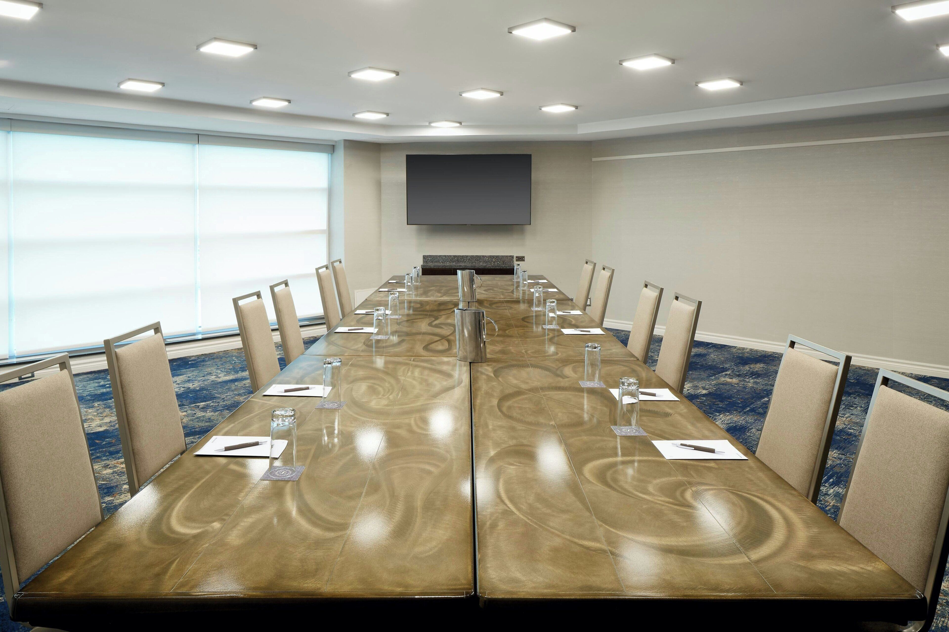 Une salle de conférence avec une longue table, des chaises, un téléviseur à écran plat et un sol recouvert de moquette.