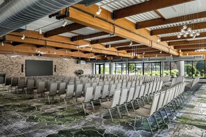 A conference room with rows of chairs, a large screen, and a view of greenery outside.