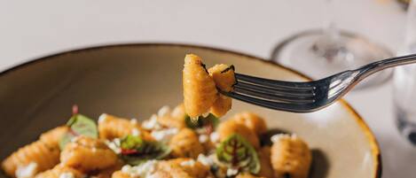 A bowl of pasta with a fork lifting a piece, accompanied by a glass of red wine and a water glass on a table.