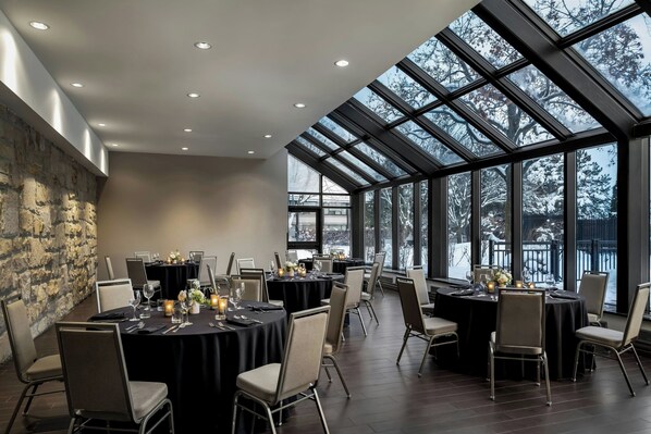 A spacious dining area with round tables, chairs, and a stone wall.