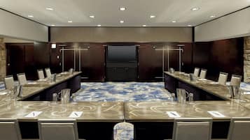 Un salón de conferencias con una larga mesa, sillas y una pantalla grande.