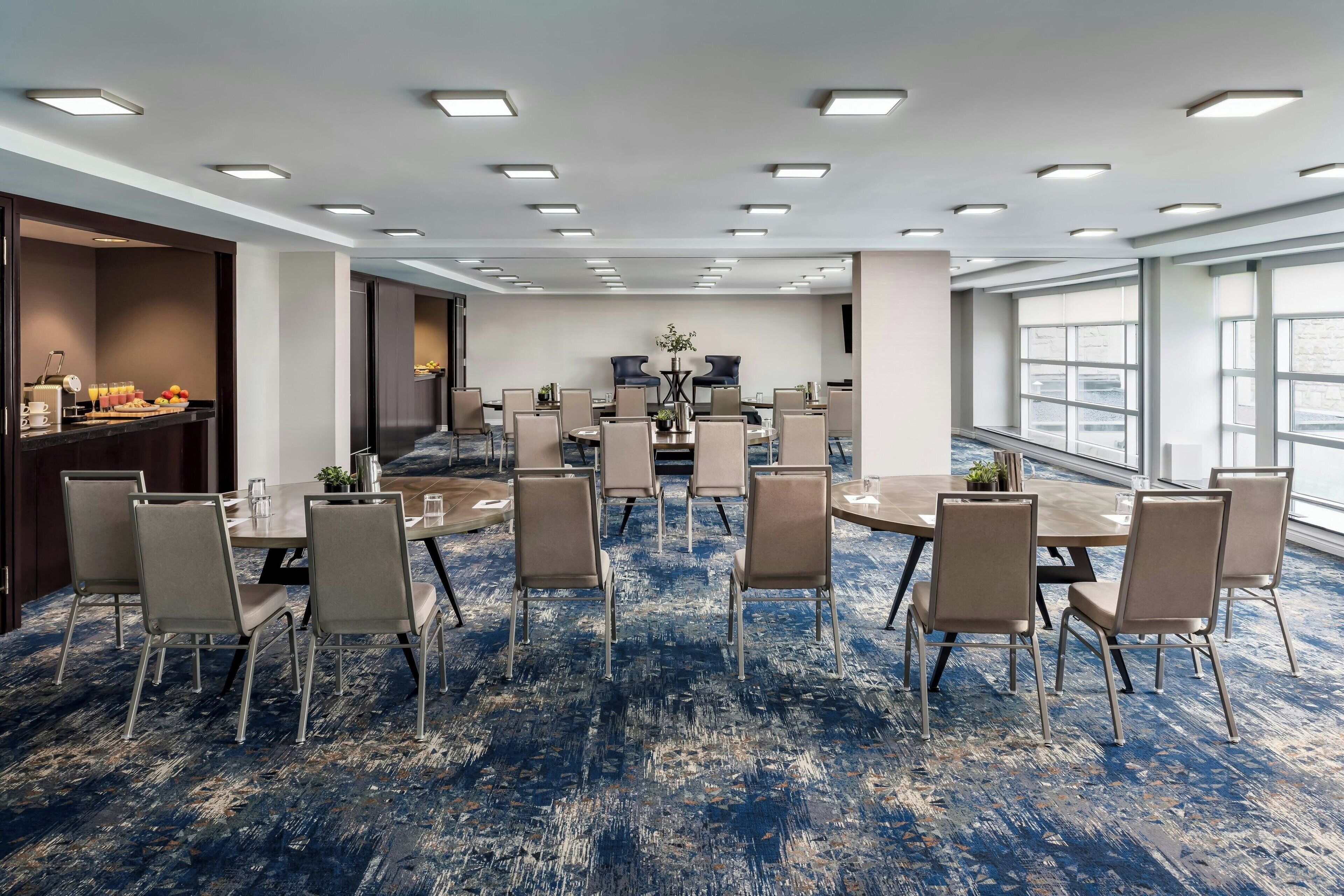 Uma sala de conferências com carpete azul, mesas redondas e cadeiras bege.