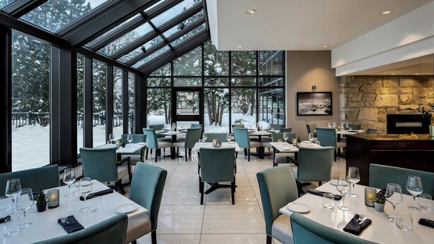 Een restaurant met een hoge plafond, grote ramen en een stenen open haard. Tafels zijn gedekt met borden, glazen en bestek.