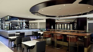 Een modern restaurant met een bar, zitplaatsen en een zichtbare keuken op de achtergrond.