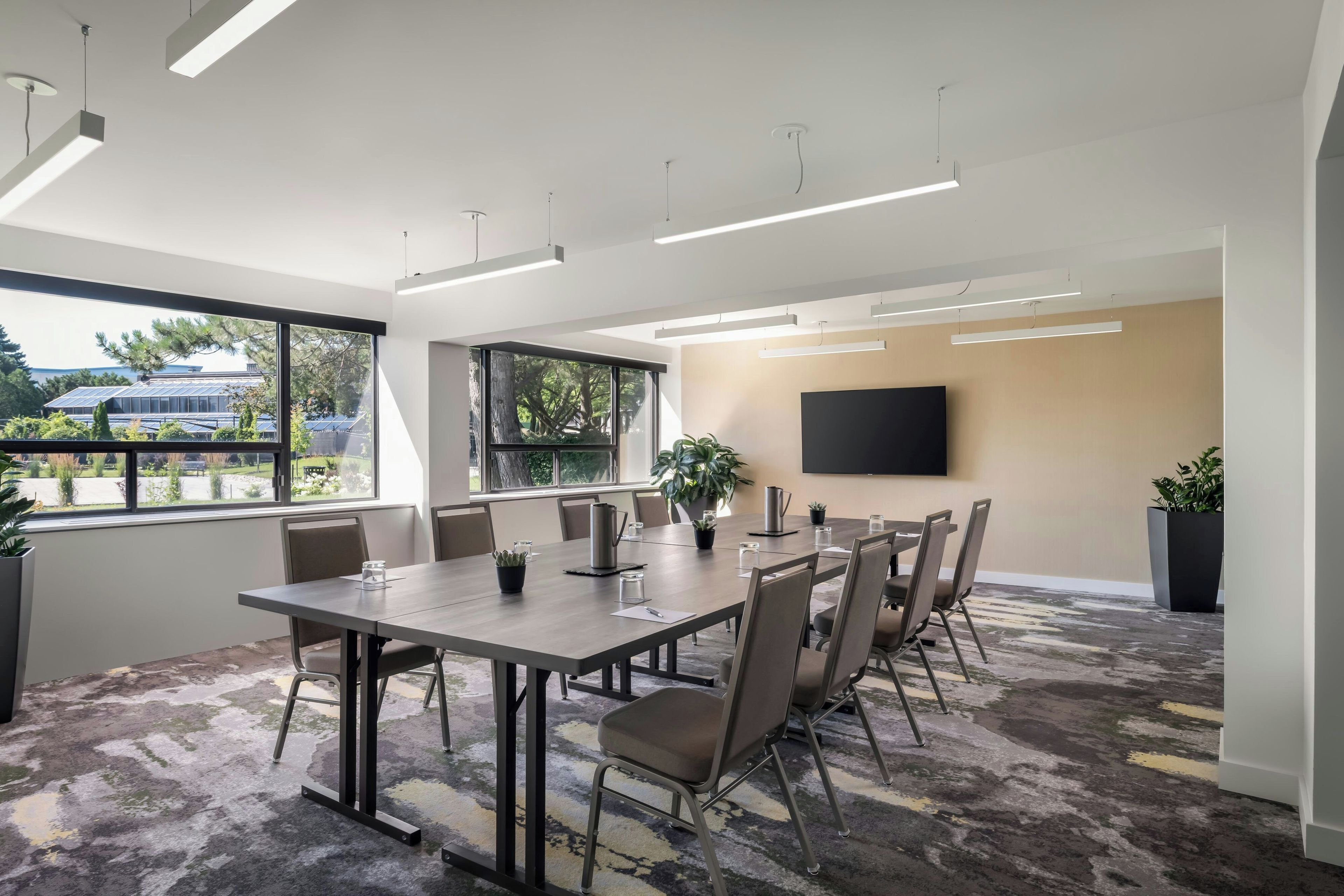Una sala de conferencias moderna con una gran mesa, sillas, un televisor de pantalla plana y ventanas amplias con vistas a paneles solares exteriores.