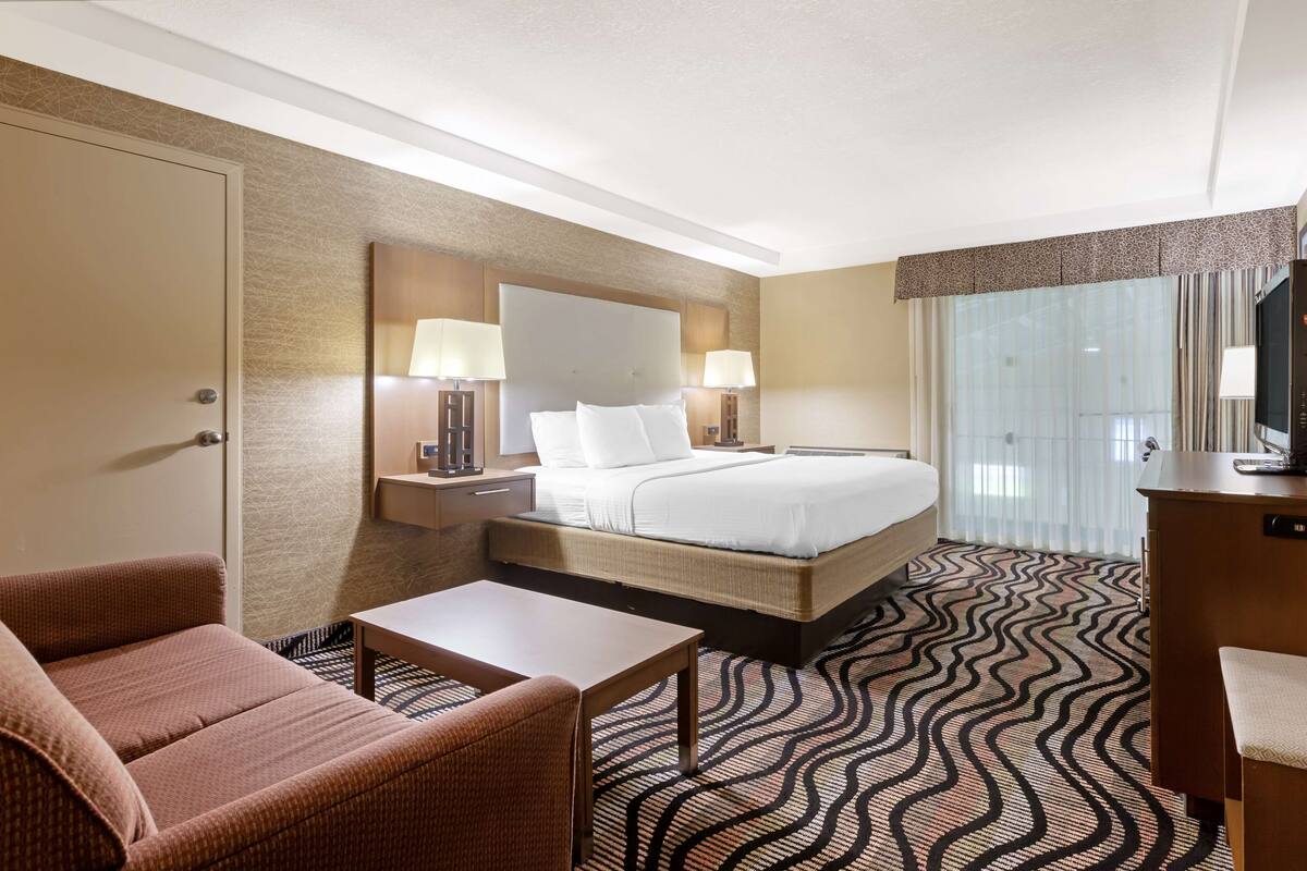 A hotel room with a bed, a desk, a chair, a TV, and a window with curtains.
