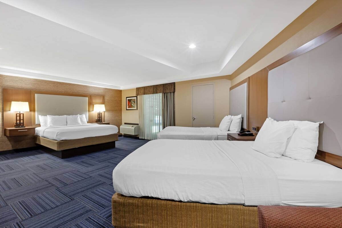 A hotel room with two beds, a large mirror, a flat-screen TV, and a desk with a lamp.