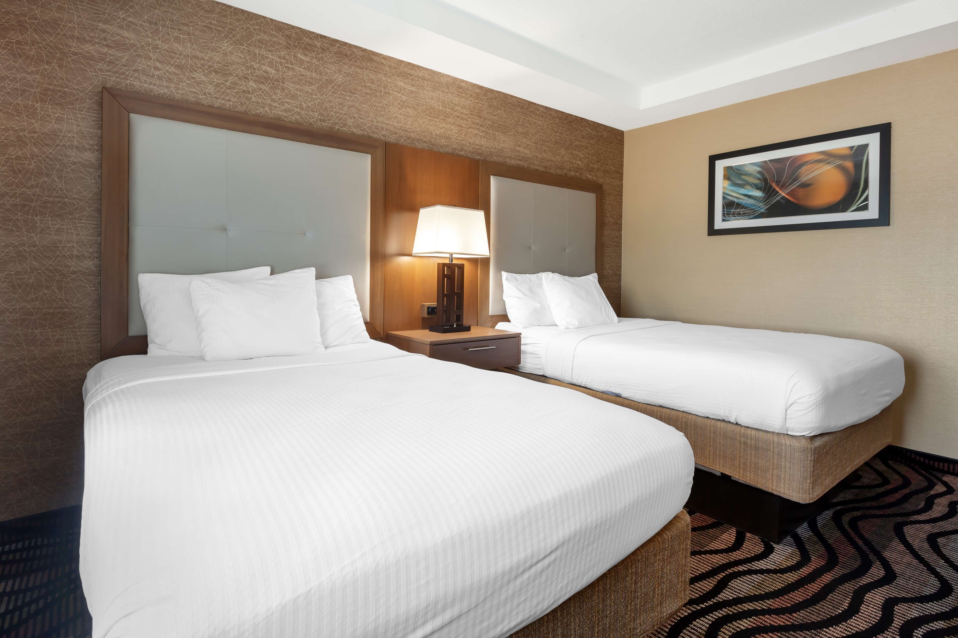 Ein Hotelzimmer mit zwei Betten, einem Nachttisch mit Lampe, einem gerahmten Bild an der Wand und einem gemusterten Teppich.