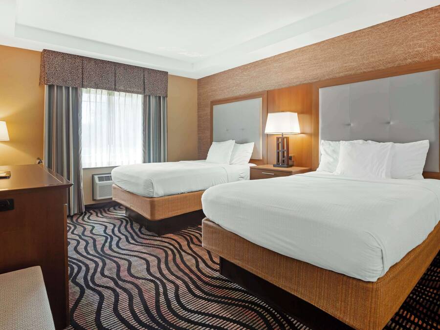 A hotel room with two beds, a desk, a TV, and a patterned carpet.