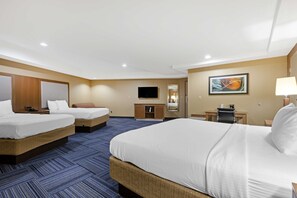 A hotel room with three beds, a TV, a desk, and a lamp.