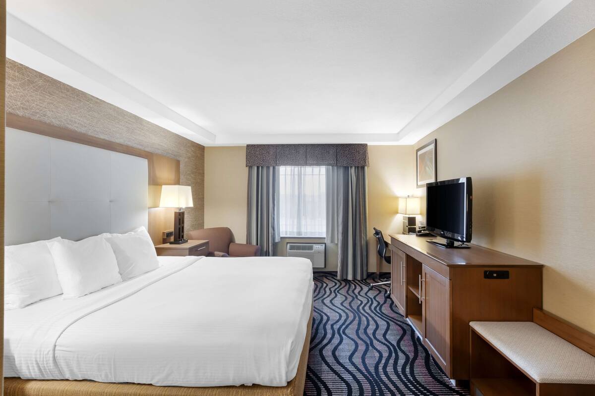 A hotel room with a large bed, a desk with a television, a chair, and a window with curtains.