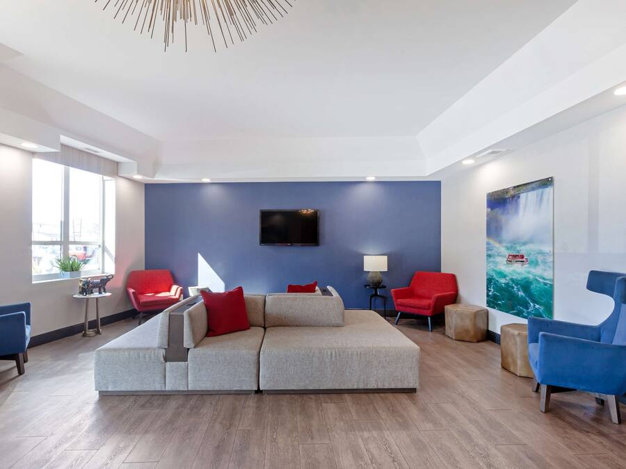 A modern living room with a sectional sofa, red chairs, a flat-screen TV, and a large window.