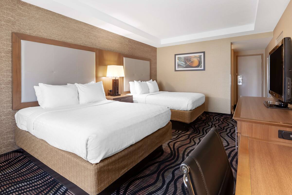 A hotel room with two beds, a desk, a television, and a patterned rug.