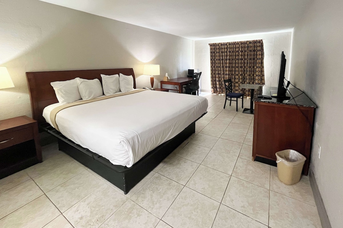 A hotel room with a large bed, a desk, a chair, and a computer.