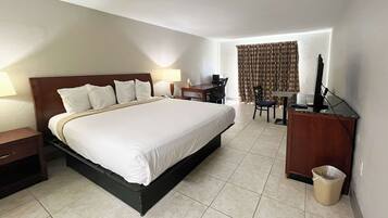A hotel room with a large bed, a desk, a chair, and a computer.
