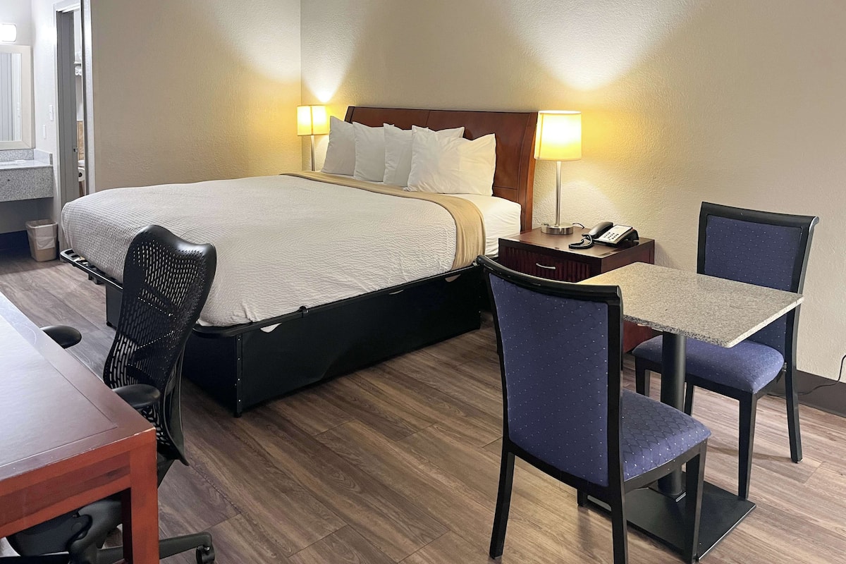 A hotel room with a bed, two bedside lamps, a desk with a chair, and a small table.
