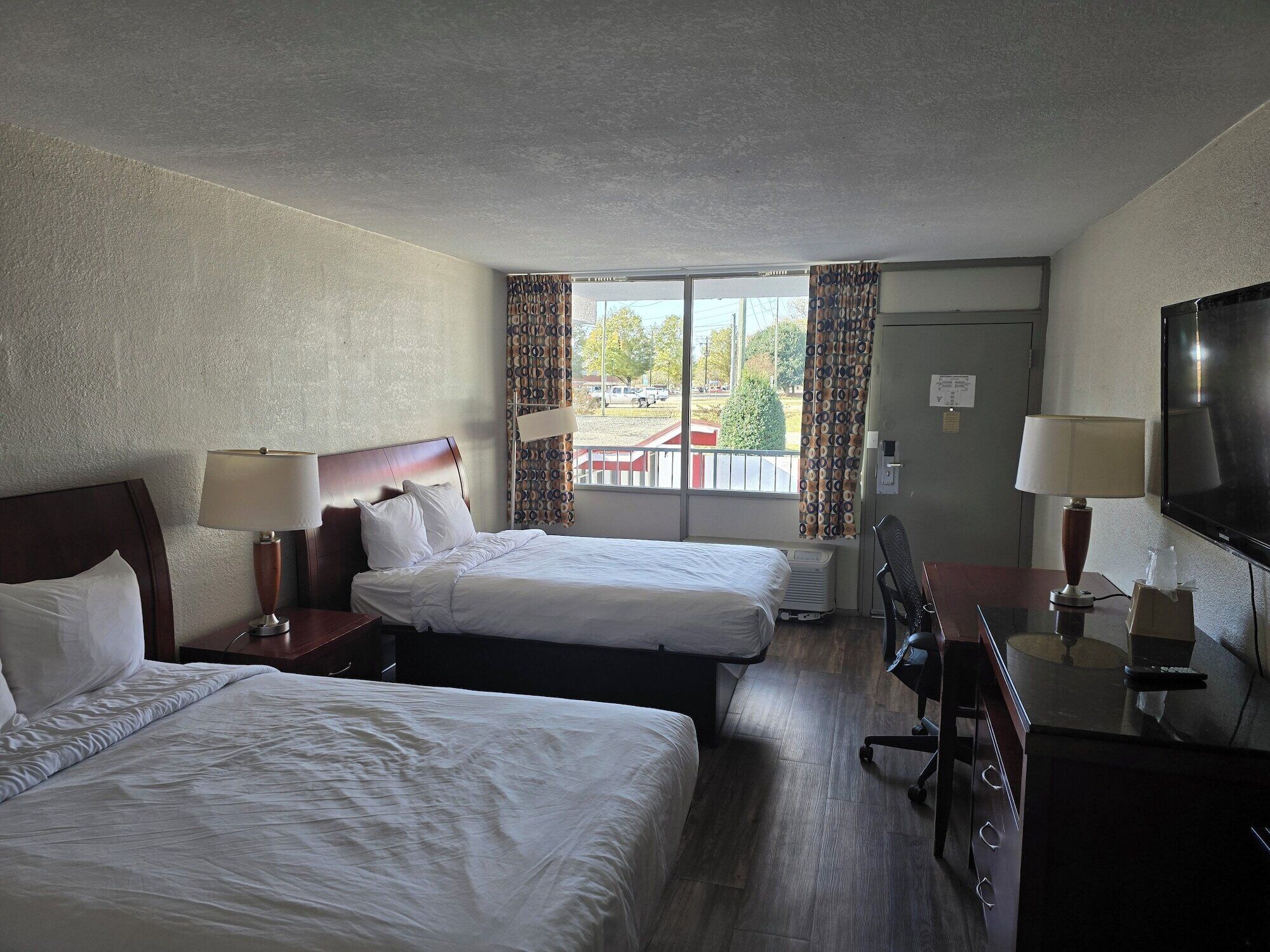 A hotel room with two beds, a desk with a chair, a TV, and a window with curtains.