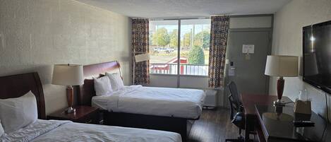 A hotel room with two beds, a desk with a chair, a TV, and a window with curtains.