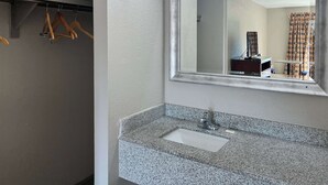 Ein Badezimmer mit Waschbecken aus Granit, einem Spiegel mit Beleuchtung darüber und Holzaufhängern an einem Kleiderständer.
