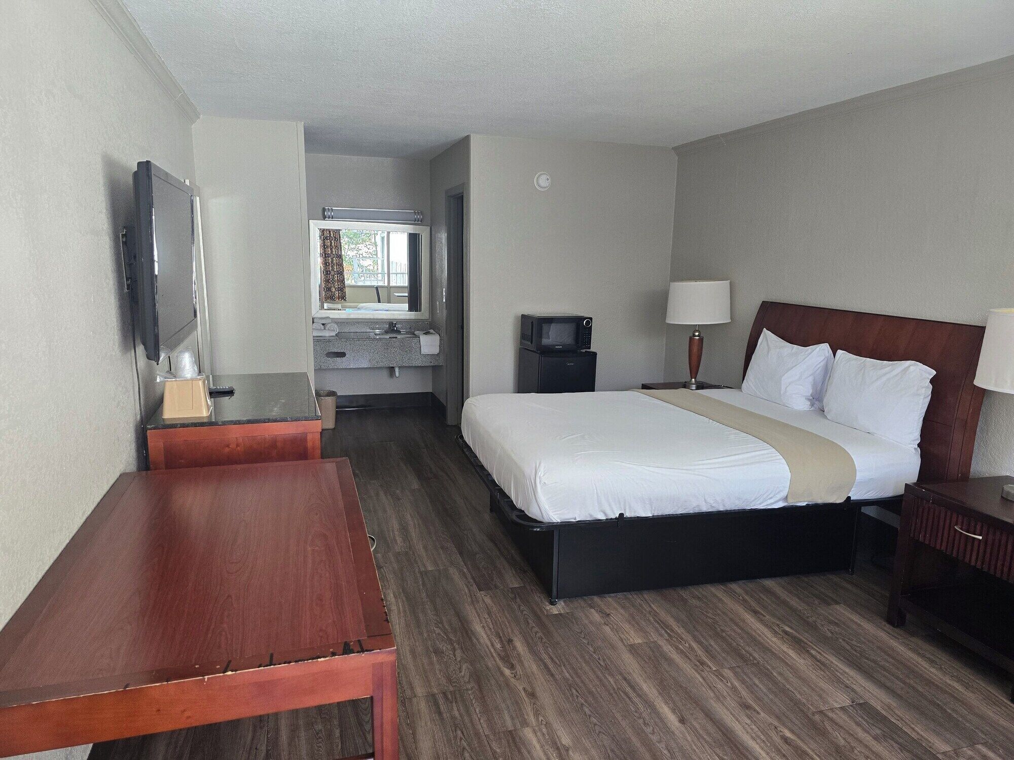 A hotel room with a bed, bedside table, desk, TV, and a small kitchenette area with a microwave.