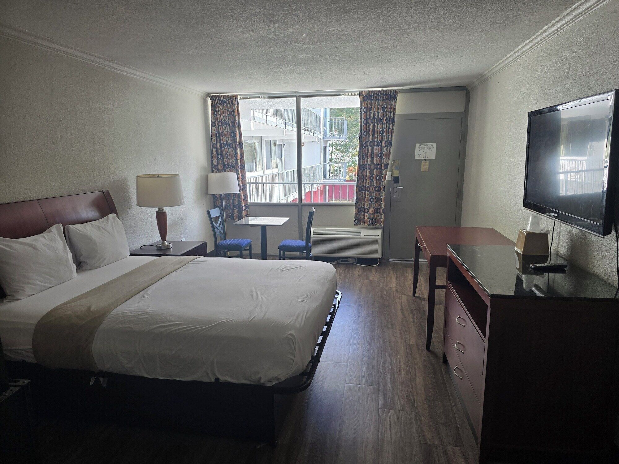 A hotel room with a large bed, a desk, a chair, a television, and a window with curtains.