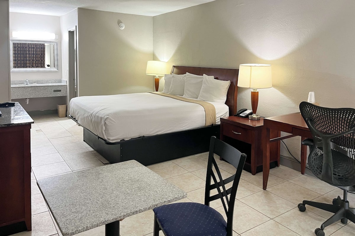 A hotel room with a bed, bedside lamps, a desk with a chair, and a small table.