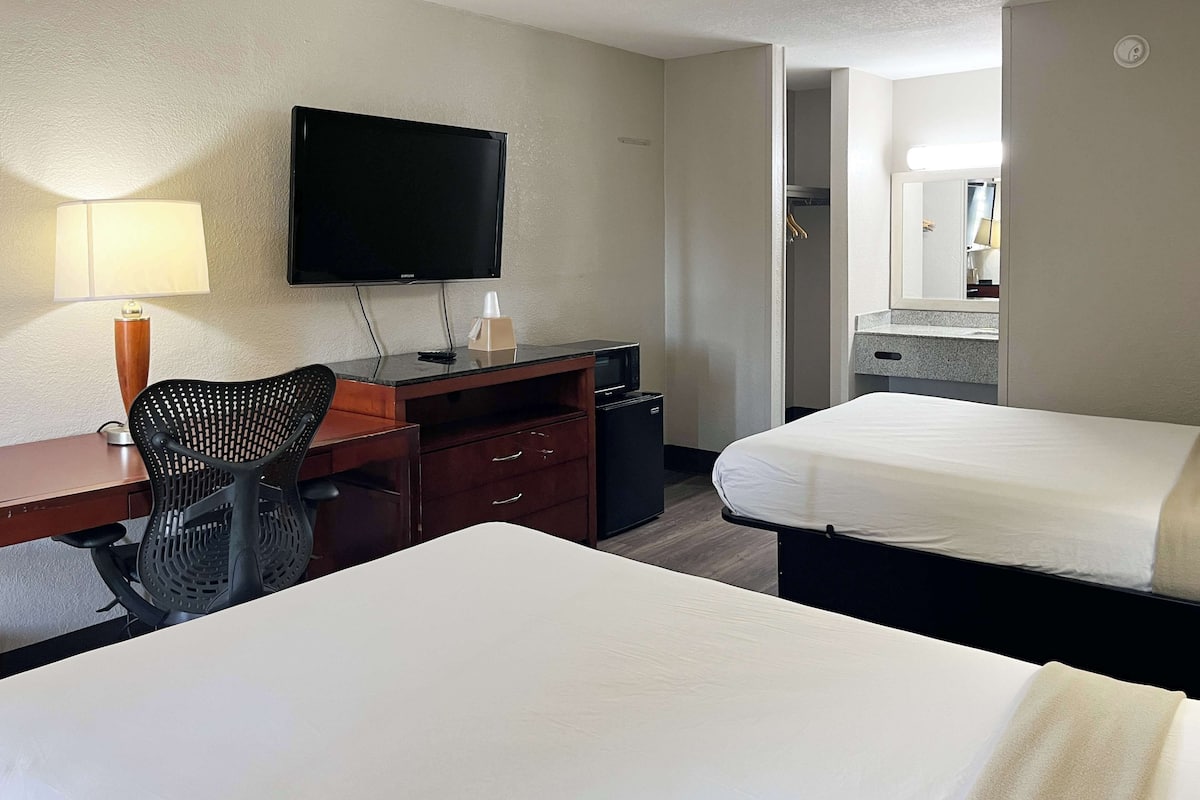 A hotel room with two beds, a desk with a chair, a television, and a small refrigerator.